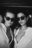 Black and white photo of two women wearing Ray Ban sunglasses and open white shirts, styled like a film still from a fashion-forward AI shoot