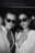 Black and white photo of two women wearing Ray Ban sunglasses and open white shirts, styled like a film still from a fashion-forward AI shoot