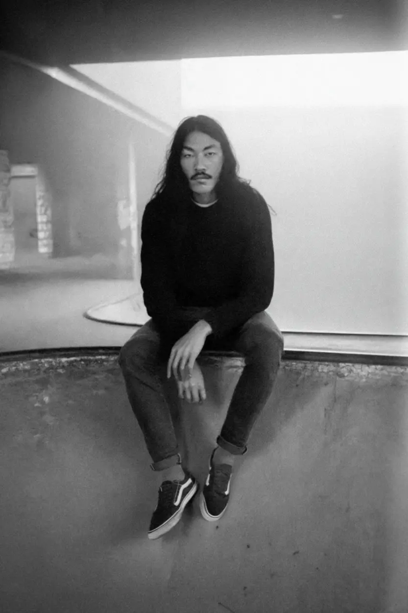 AI-crafted image of a long-haired man sitting on a skate pool edge, wearing Vans and staring directly at the viewer